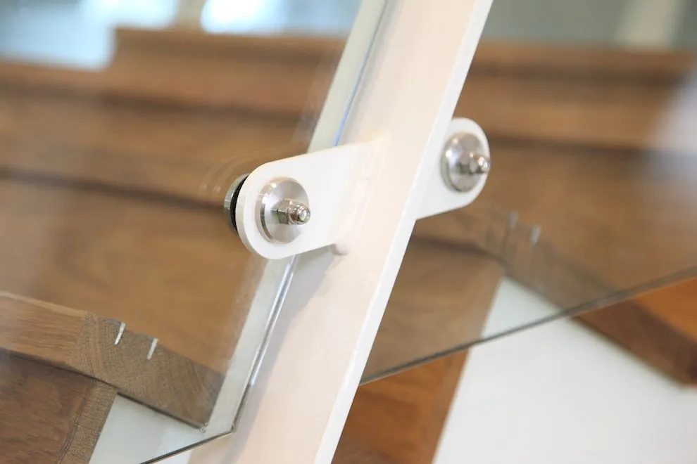 Stainless steel fixings holding a glass balustrade panel to a white steel stair