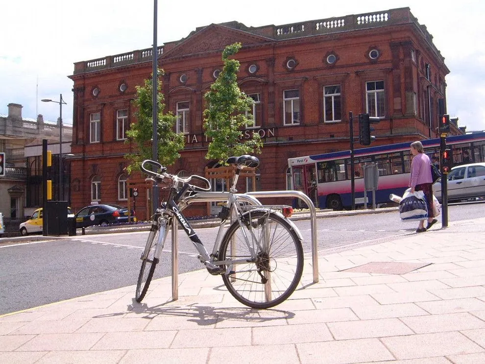 Bicycle locked to a stainless steel Sheffield stand outside a red-brick building in Norwich