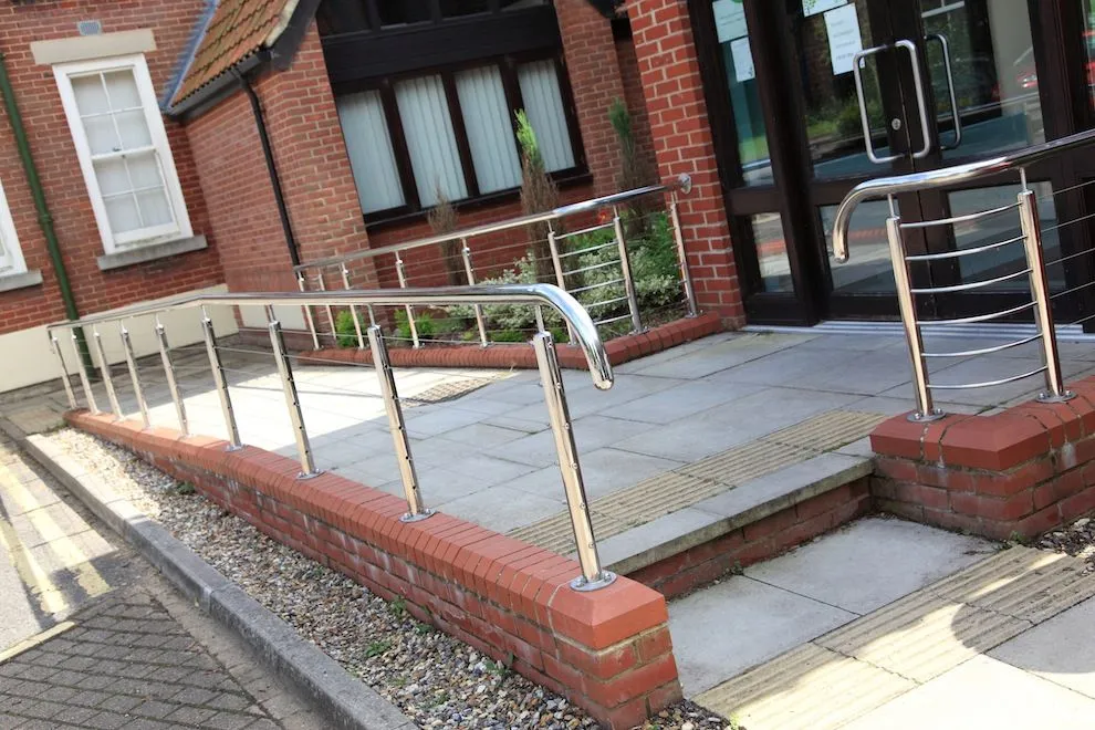Polished stainless steel handrails on a brick-edged entrance ramp