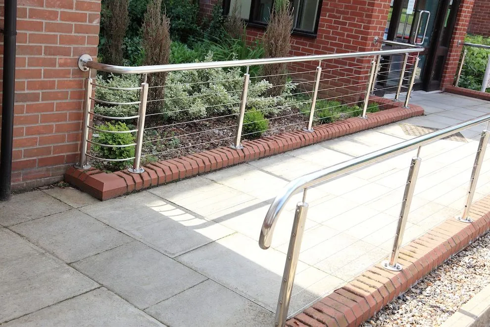Stainless steel handrail and wire balustrade alongside an entrance ramp and planter
