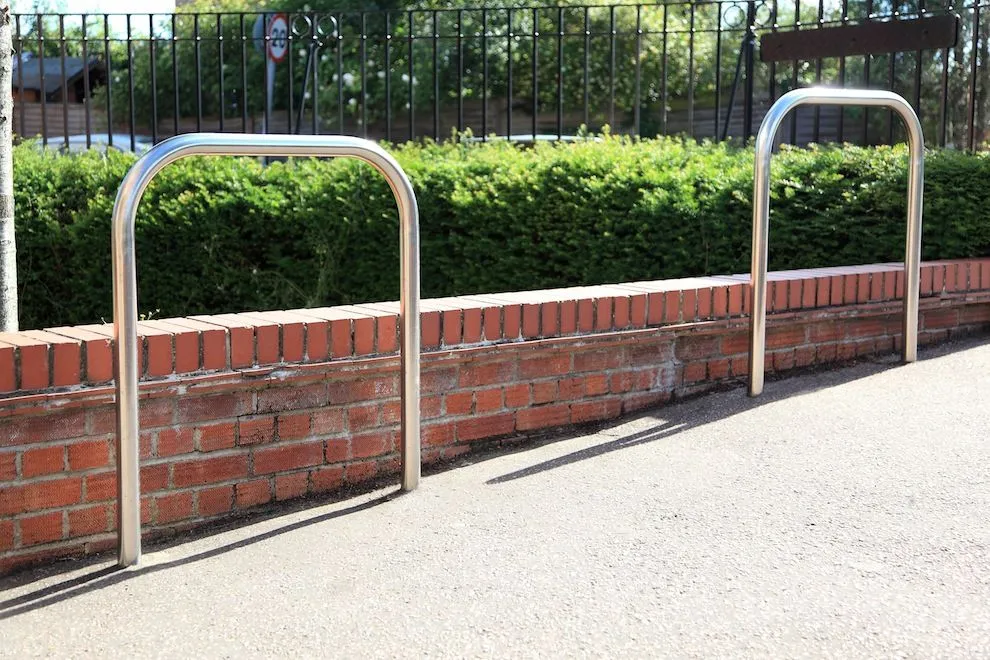 Stainless steel Sheffield cycle stands in front of a low brick wall and railings