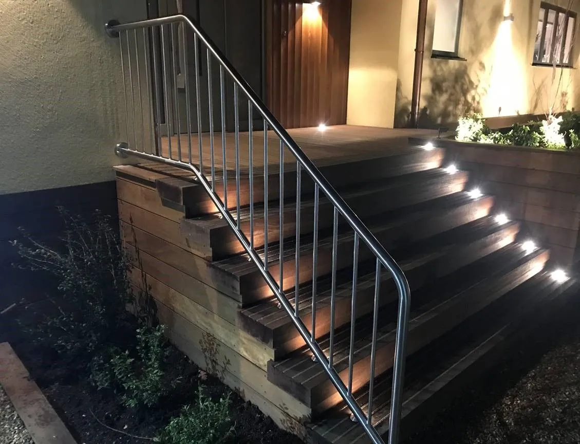 Stainless steel handrail beside lit timber steps at night