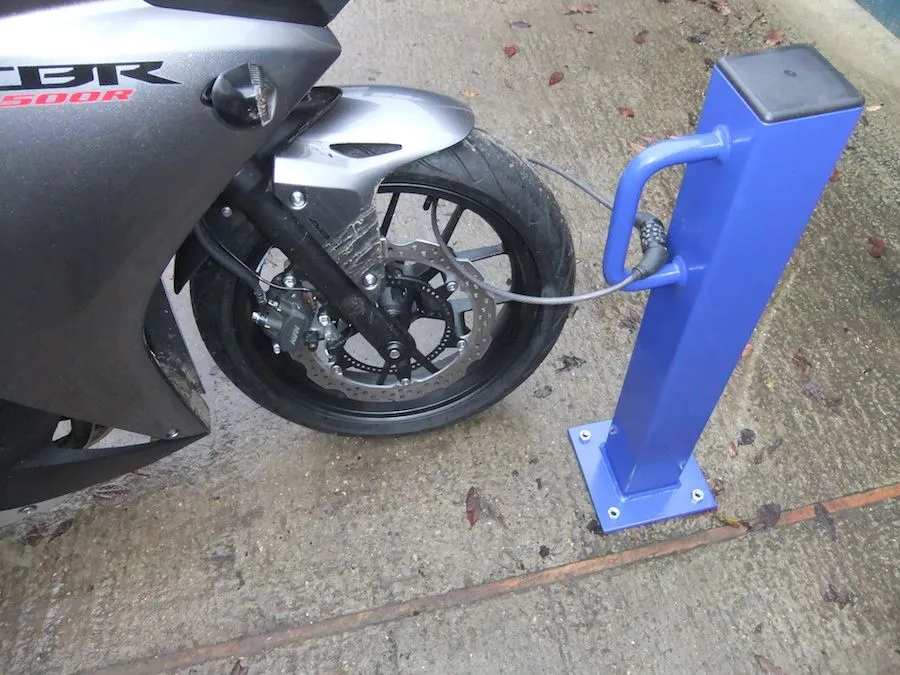 Blue steel motorcycle security post with a cable lock through a motorbike wheel