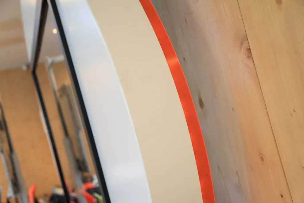 Edge of a white aluminium screen surround with an orange trim on a timber wall