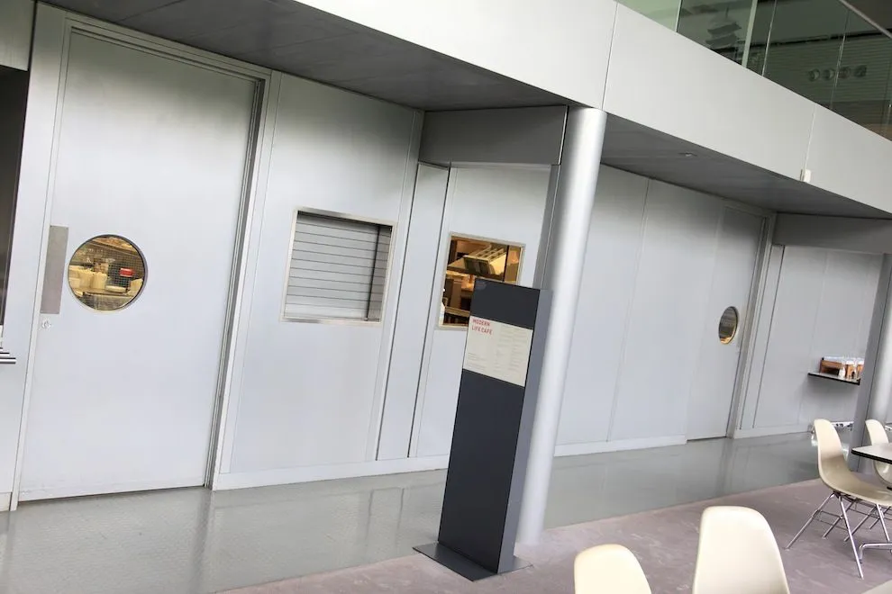 Grey steel display wall with porthole windows in a museum gallery