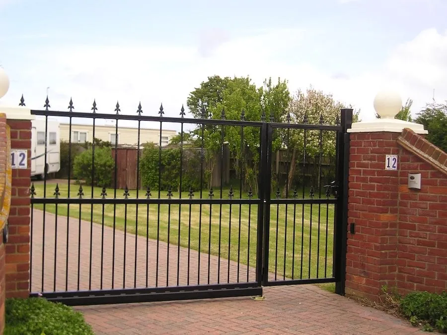 Black steel sliding gate with spear-top railings between brick pillars