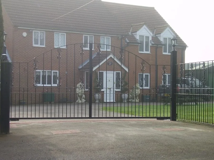Black steel arched driveway gates and railings in front of a house