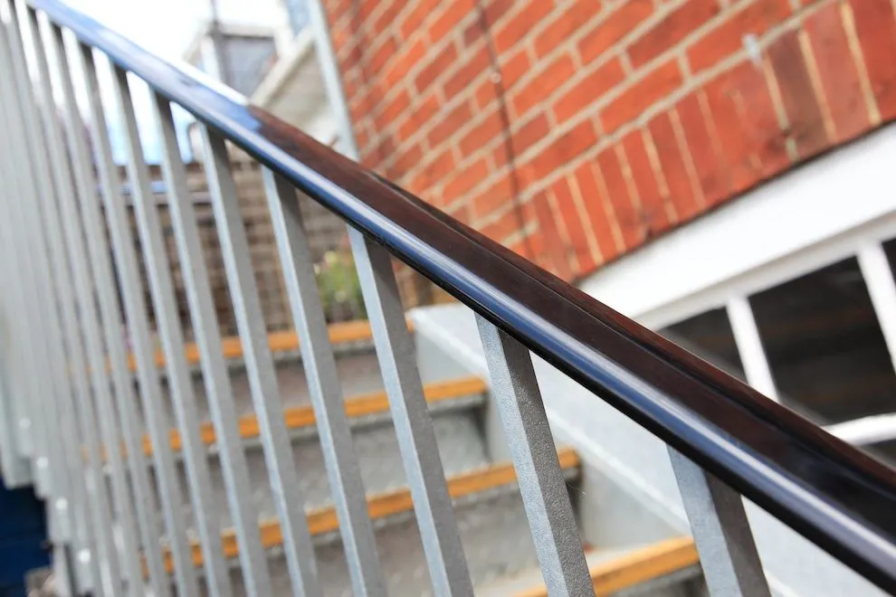 Black steel handrail on a galvanised steel staircase beside a brick building