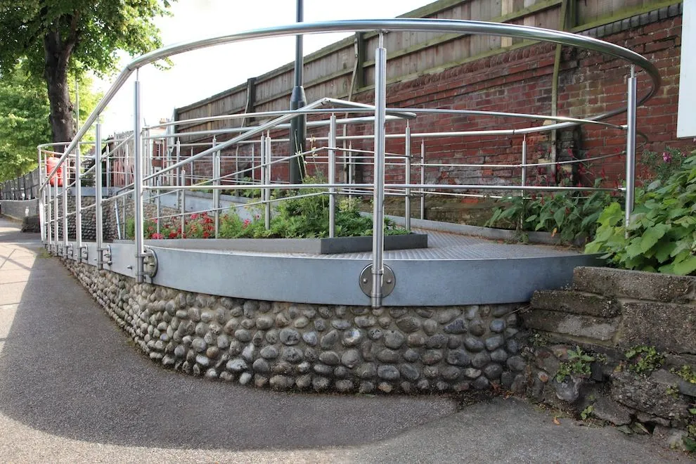 Curved stainless steel balustrade on a flint-walled raised planter