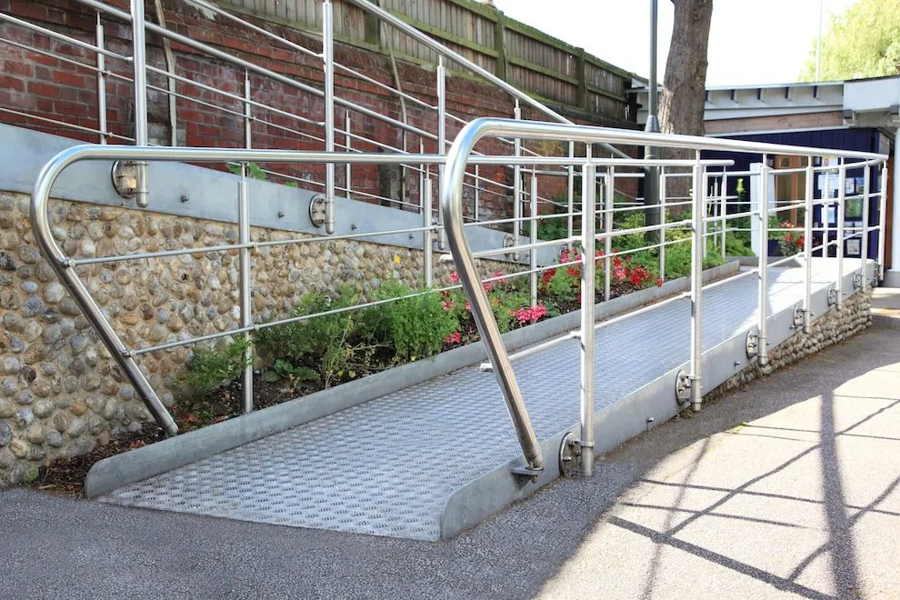 Stainless steel handrails on a sloping ramp beside a flint wall