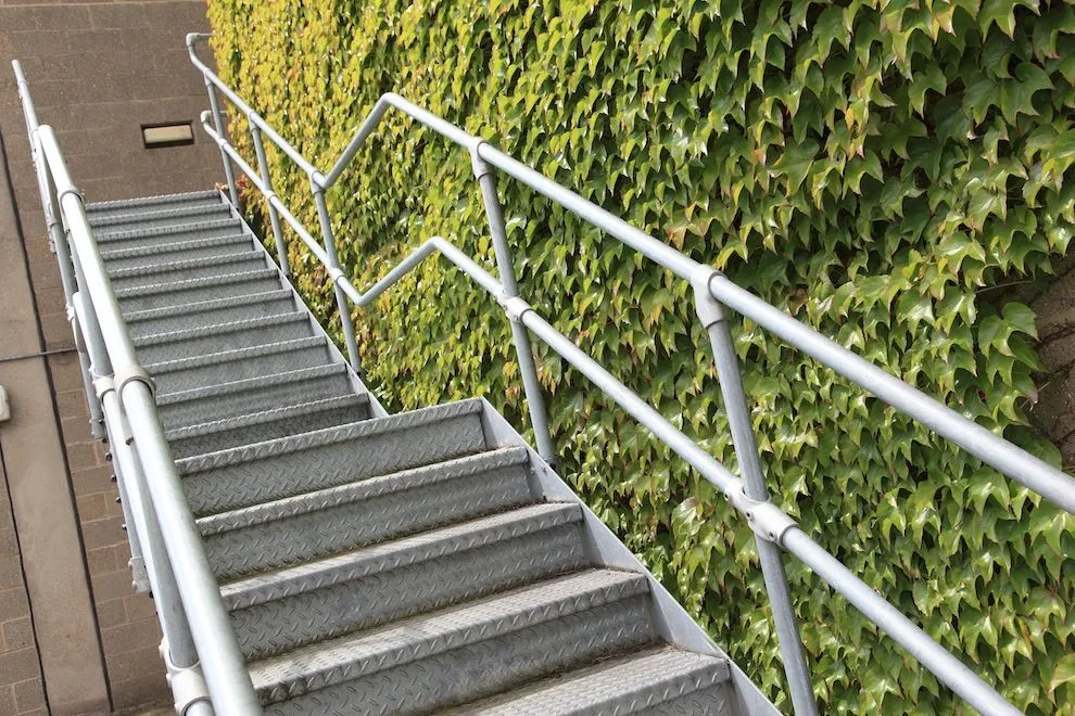 Galvanised steel staircase and handrails rising beside an ivy-covered wall