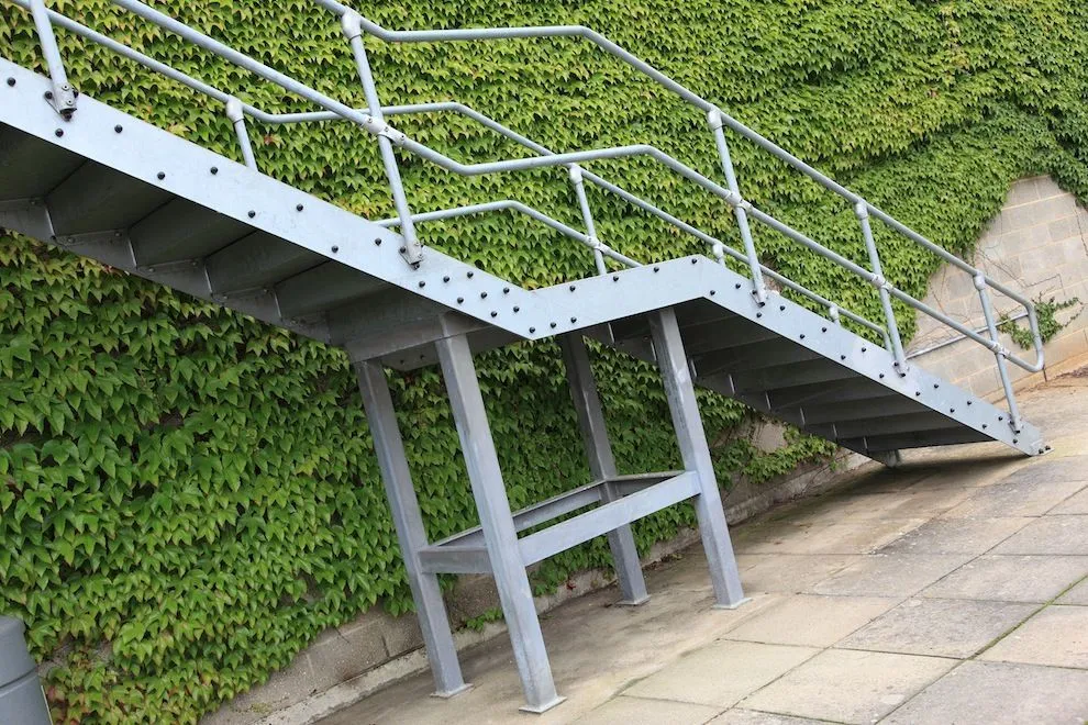 Galvanised steel external staircase with handrails against an ivy-covered wall